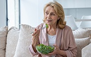 Senior woman sitting on couch eating a salad