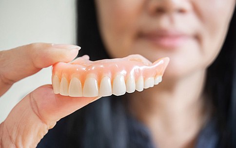 a woman holding up a denture