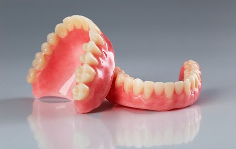 Full set of dentures resting on each other on a reflective gray surface