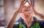 Older woman with green scarf forming a heart with her fingers to frame her eye